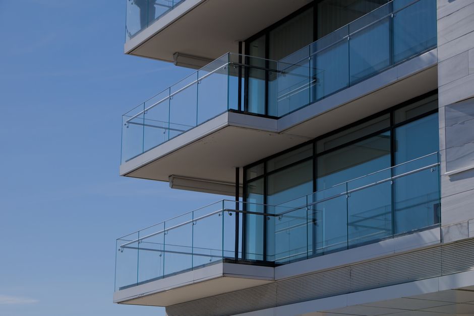 Sleek modern building with glass balconies against a clear blue sky, showcasing architectural design.