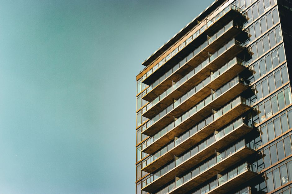 Sleek modern apartment building with glass facade and balconies, set against a clear blue sky.